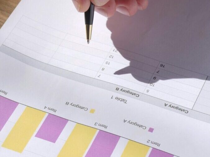 Detailed image of a hand holding a black pen writing on a document in daylight.