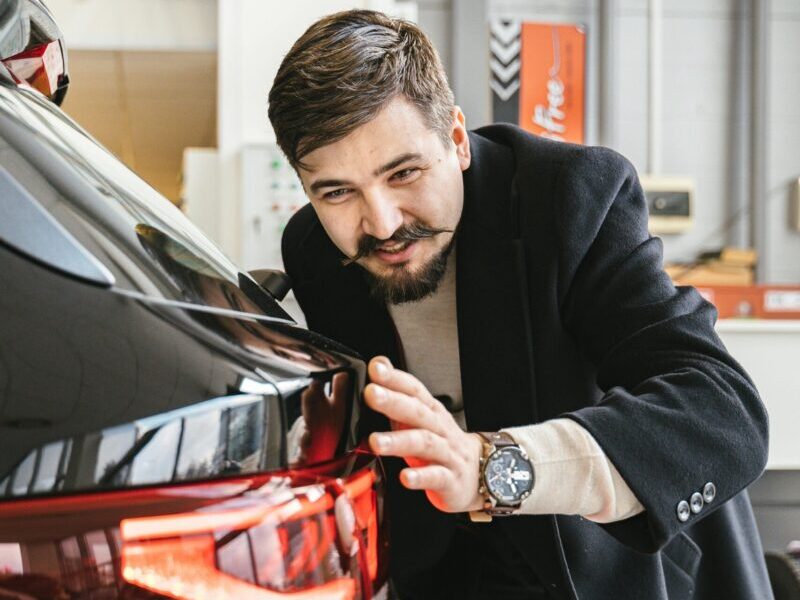 Man in business attire examining a car in an indoor setting, suggesting car maintenance or purchase.